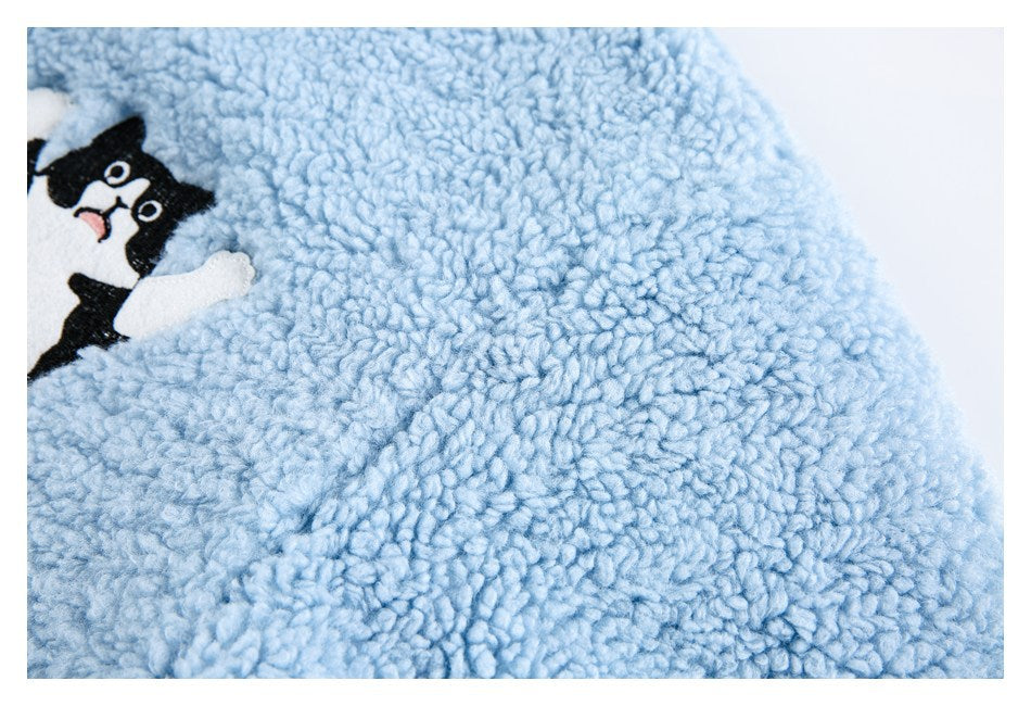Close-up of pale blue plush fabric with part of a black-and-white cat applique at the edge.