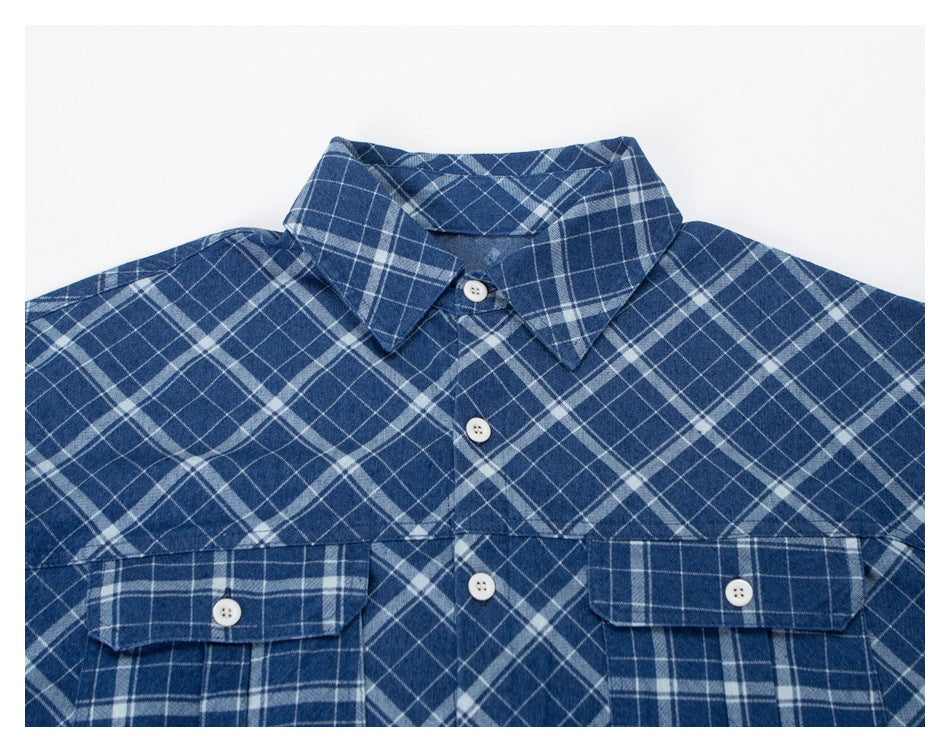 Close-up of a blue plaid shirt front, showing its pointed collar, white buttons, and two flap chest pockets.