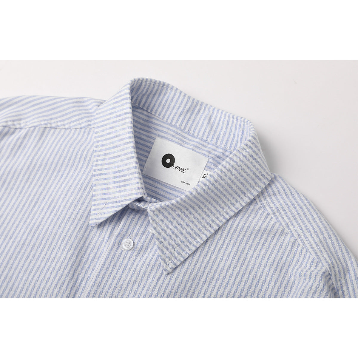 Close-up of a white shirt with fine blue stripes, showing the pointed collar and sewn-in neck label.