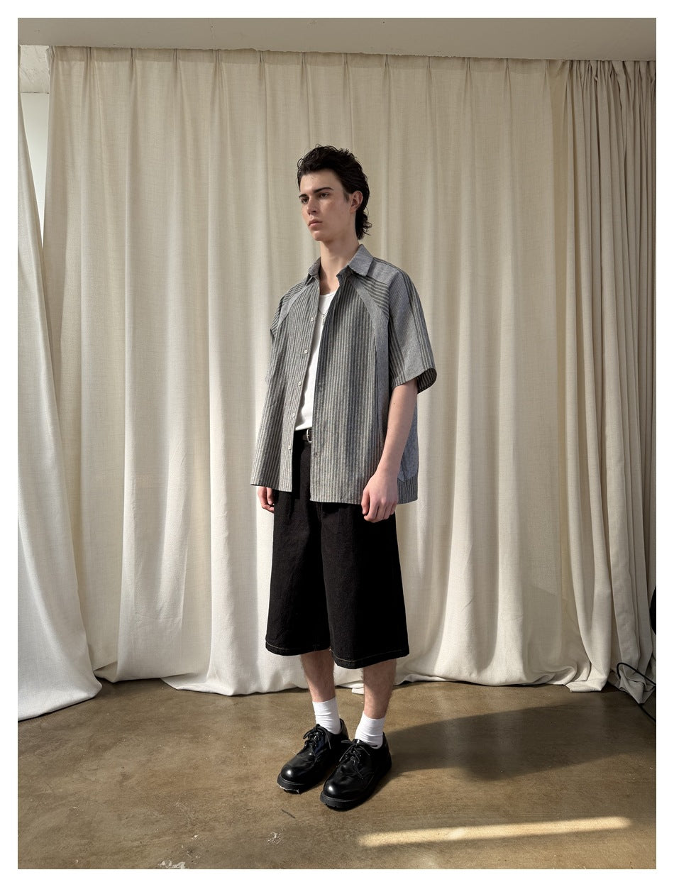 Model wearing the open striped short-sleeve shirt over a white tee with black shorts, front view