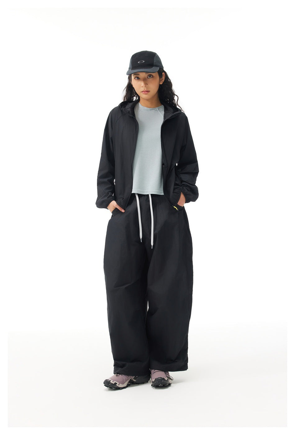 Front view of a model wearing an open black hooded jacket and loose black trousers with white drawstrings.