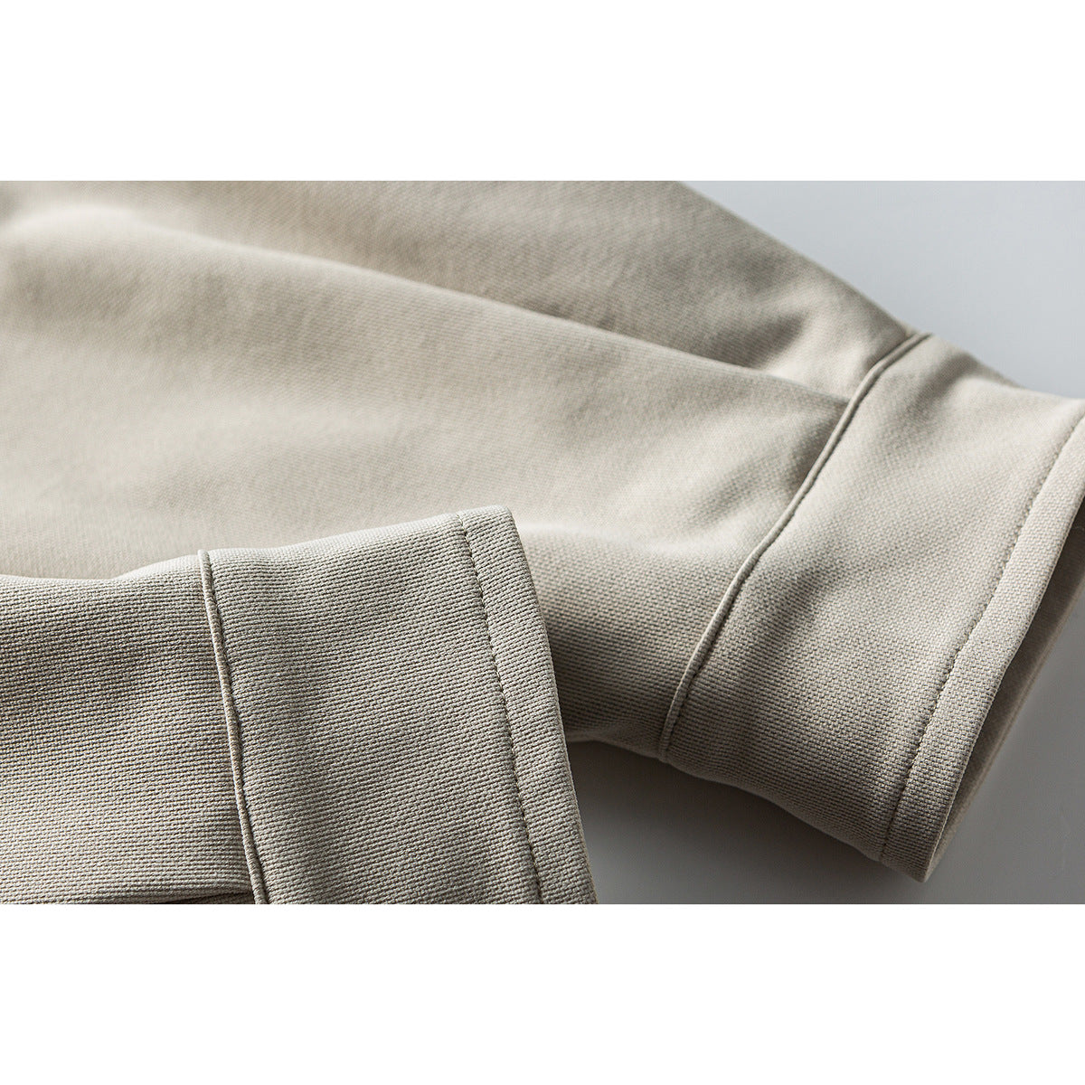 Close-up of the beige jacket's sleeve cuff and folded hem, showing stitched seams.