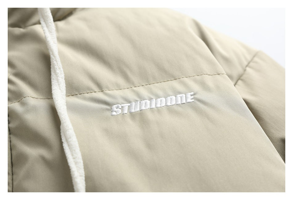 Close-up of white embroidered lettering on the chest of a beige padded jacket.