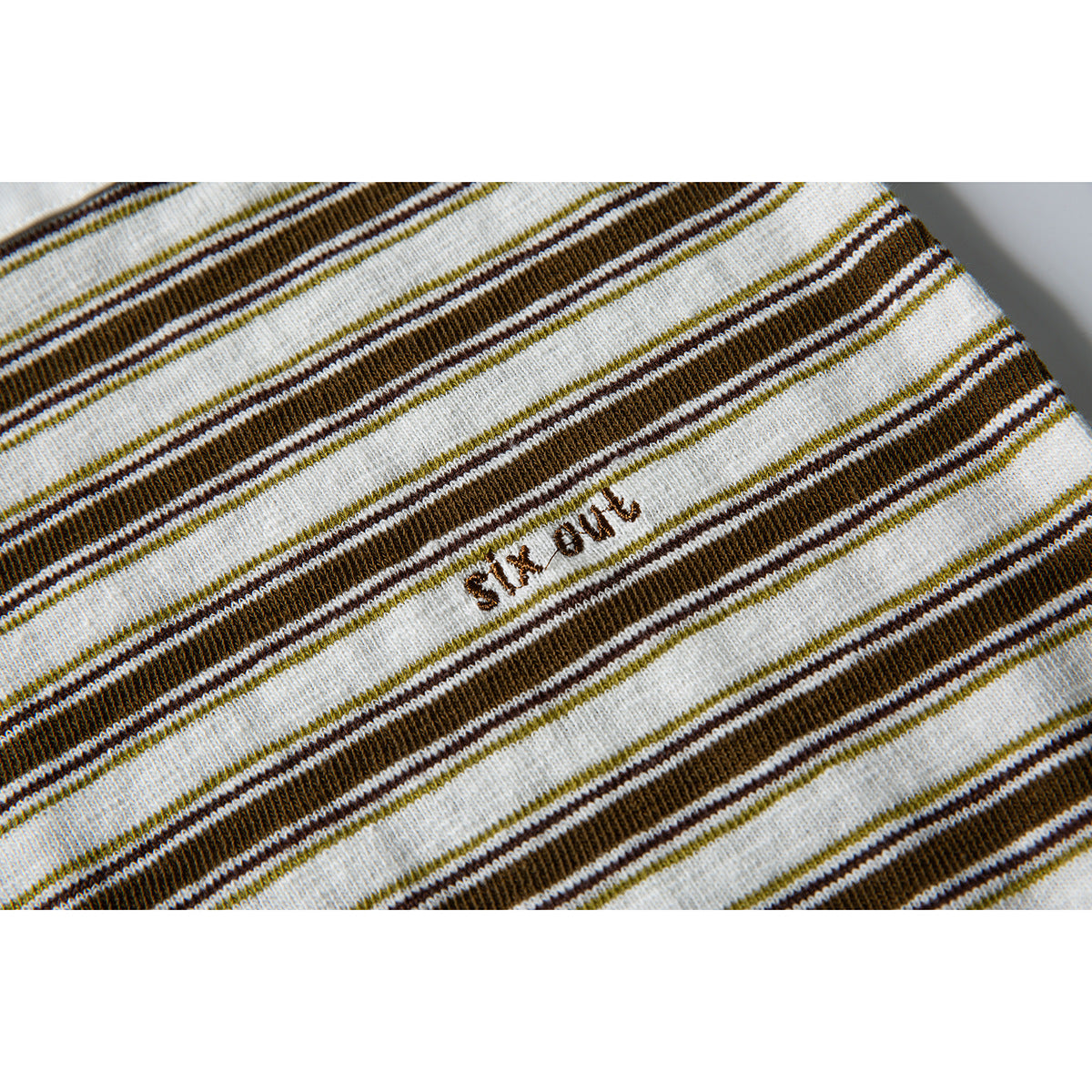 Close-up of brown, olive, and cream stripes with a small embroidered text detail on the shirt.