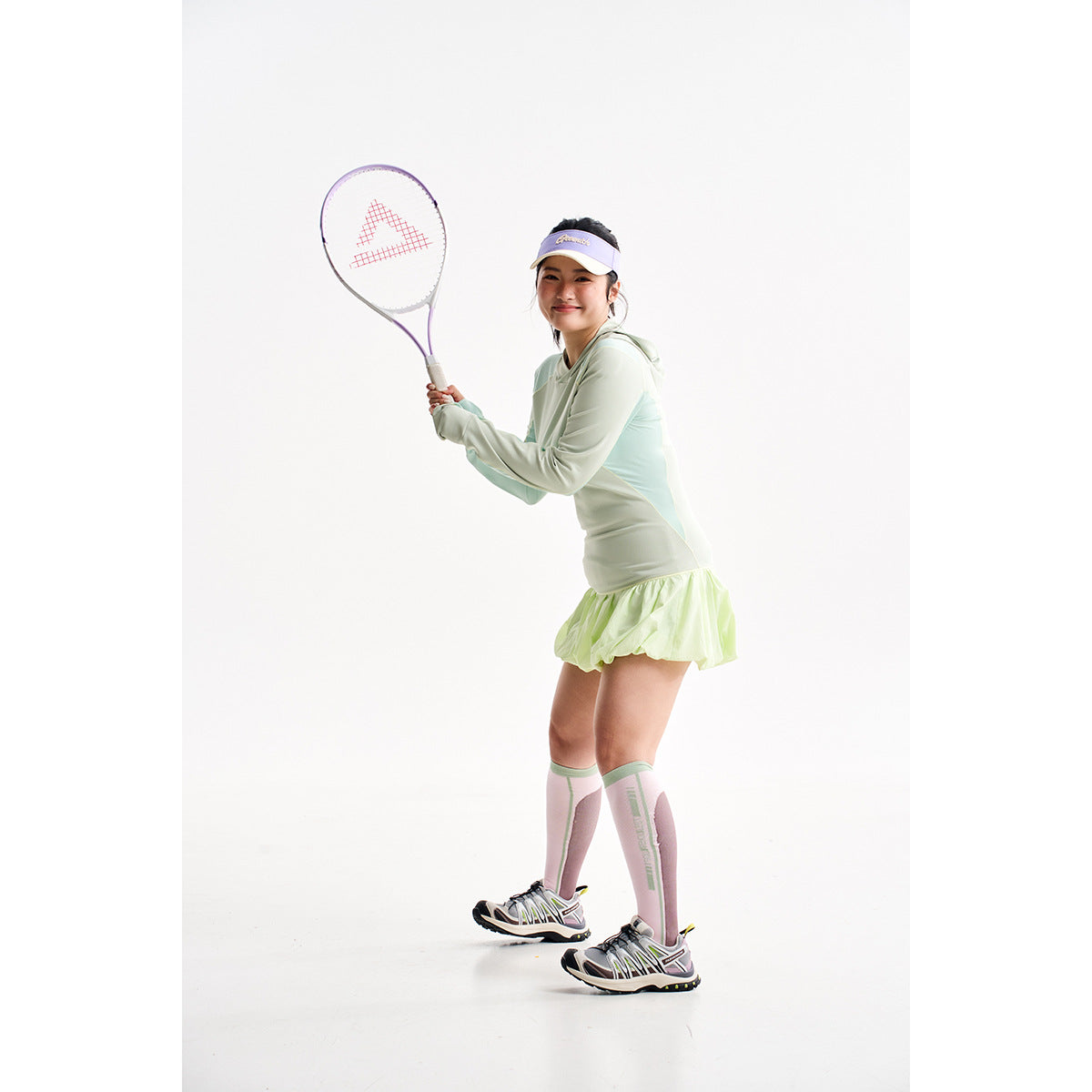 Model holding a tennis racket in a pale mint hooded top, lime skirt, and pink-and-mint knee socks.