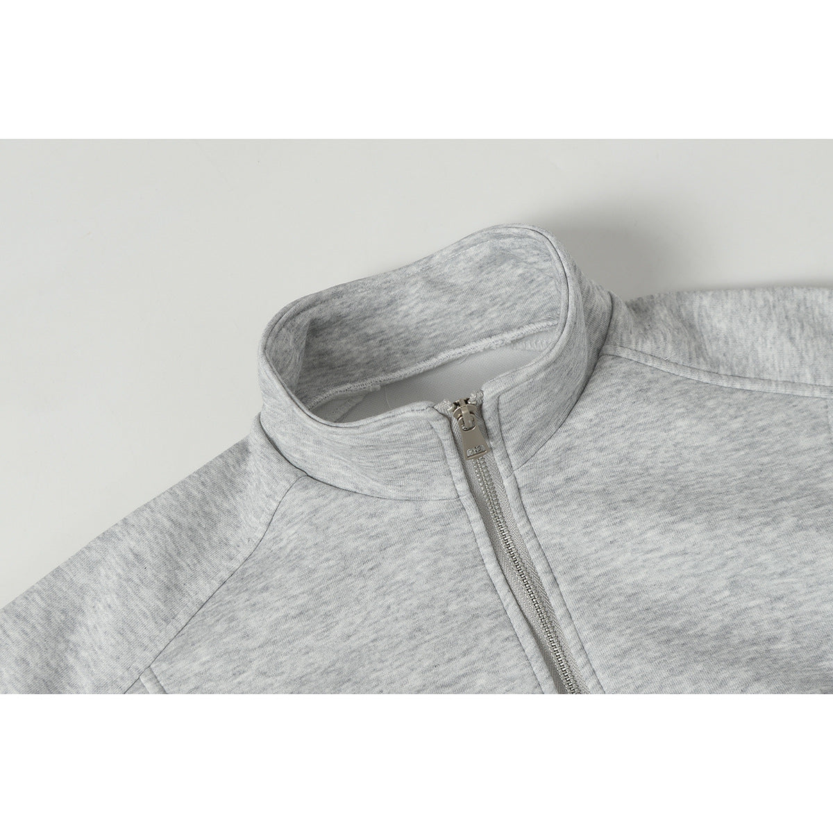 Close-up of a light gray melange jacket's stand collar and silver front zipper.