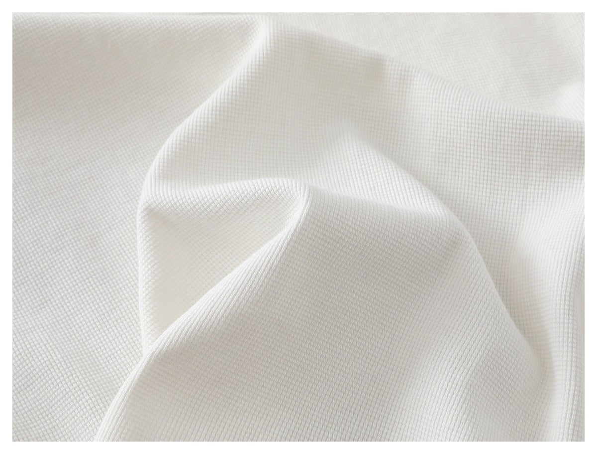 Close-up of white waffle-knit fabric draped into soft folds, showing its textured surface.