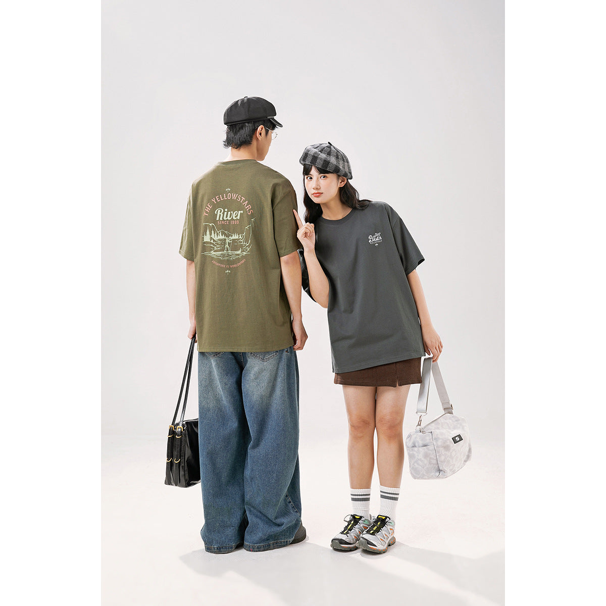 Two models show the olive T-shirt's large back graphic and the charcoal T-shirt's small front chest graphic.