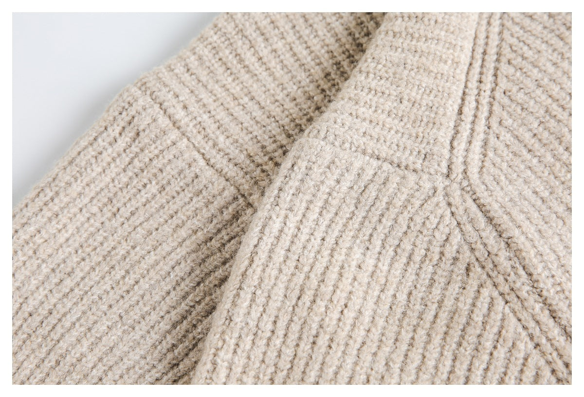 Close-up of beige chunky knit fabric with overlapping folds and visible seam lines.