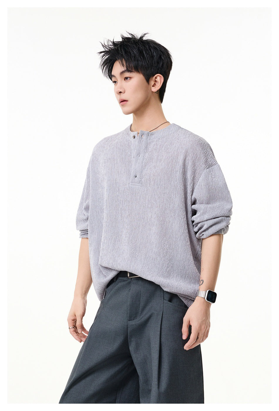 Model wearing a light gray oversized long-sleeve henley with the sleeves pushed up and dark trousers.