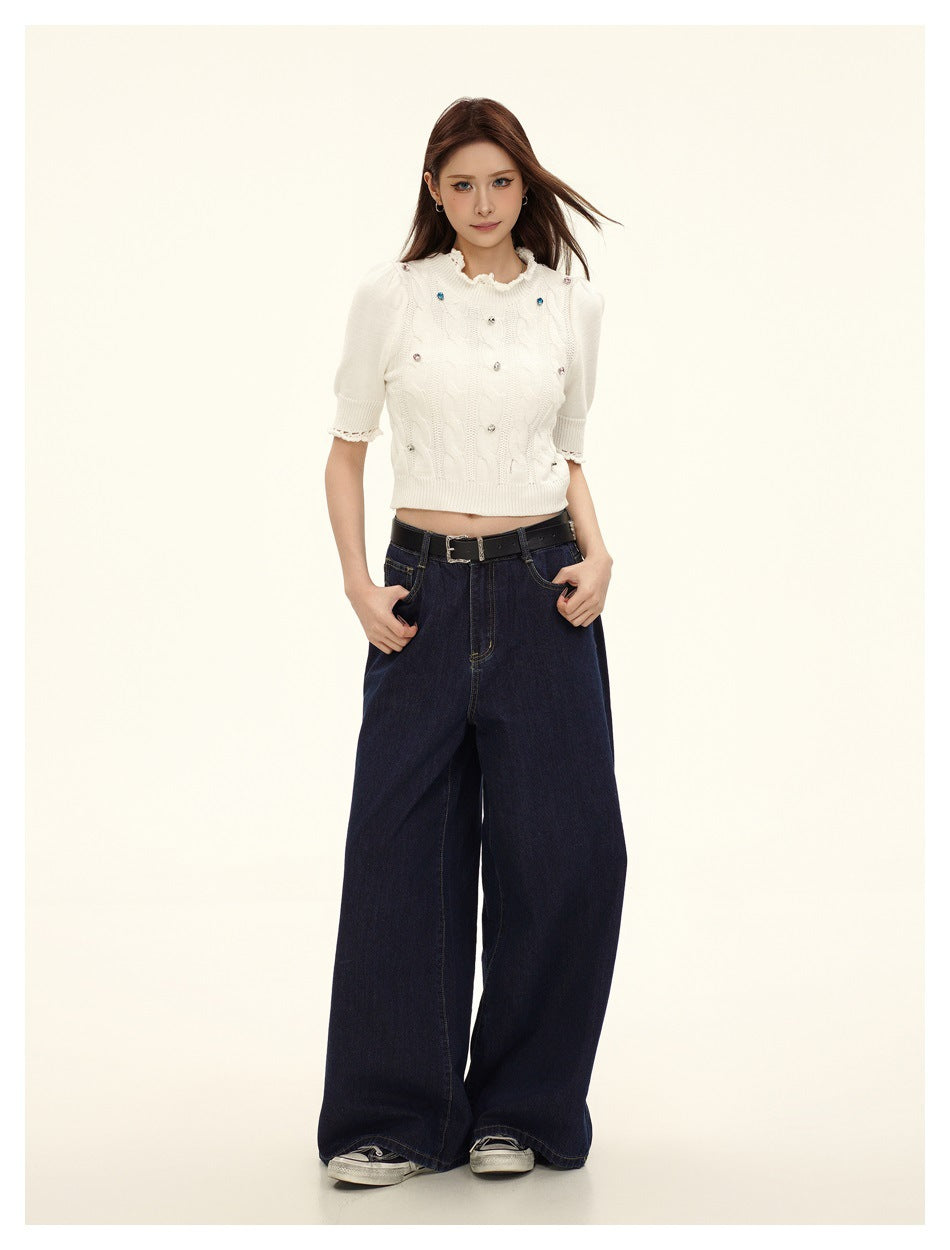 Model wearing a cream cable-knit cropped short-sleeve top with gem details and wide-leg dark blue jeans