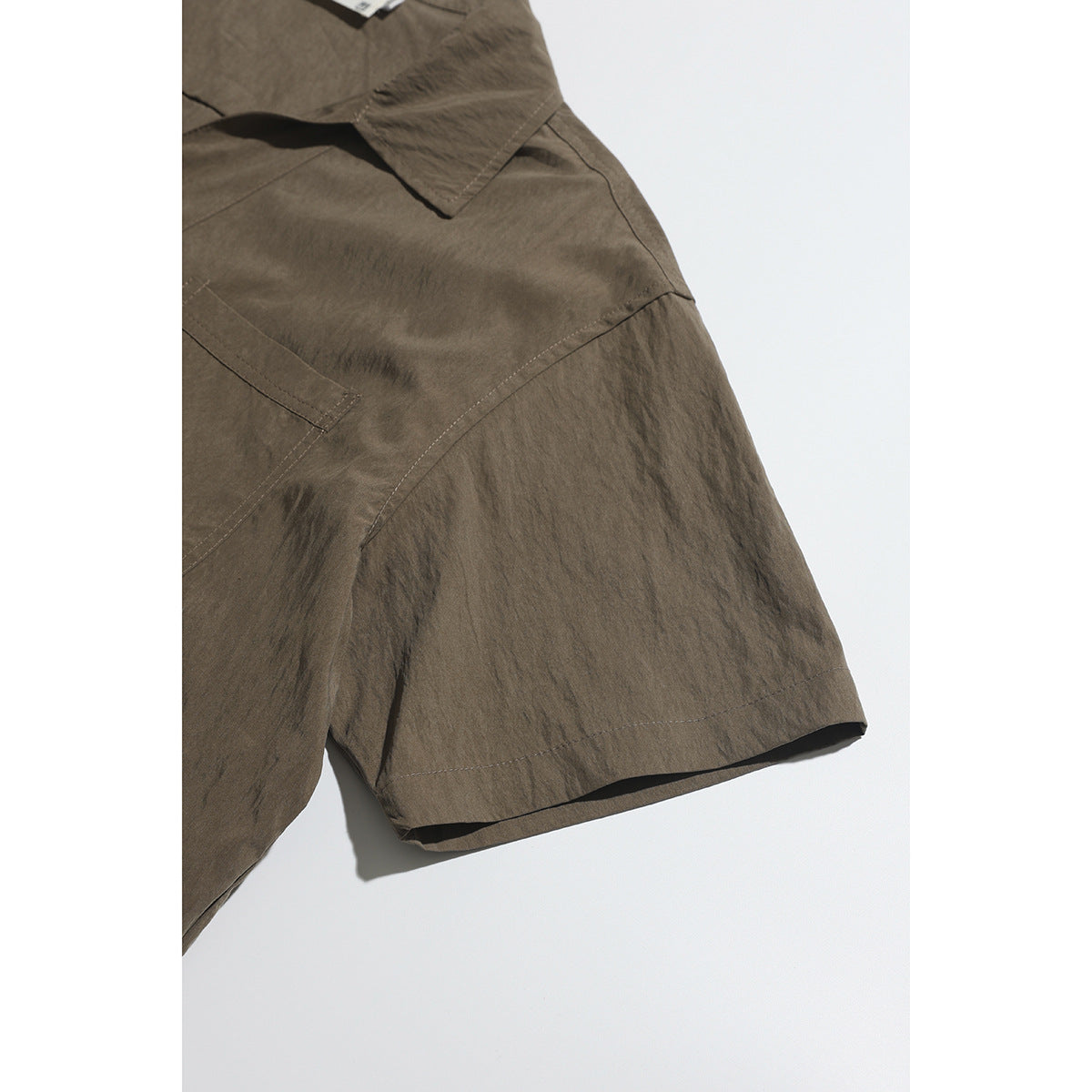 Close-up of the brown shirt's short sleeve, hem stitching, and part of its chest pocket and collar.