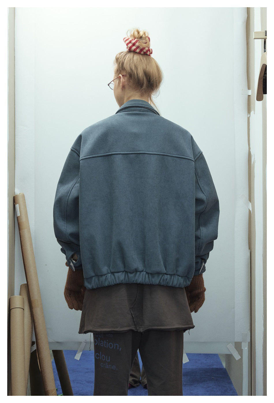 Rear view of a person wearing an oversized slate-blue jacket with a wide back seam and elastic hem.