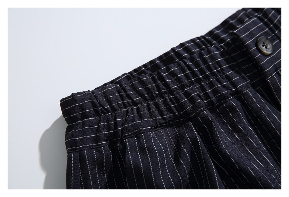 Close-up of dark pinstriped trousers showing the gathered elastic waistband and a button.