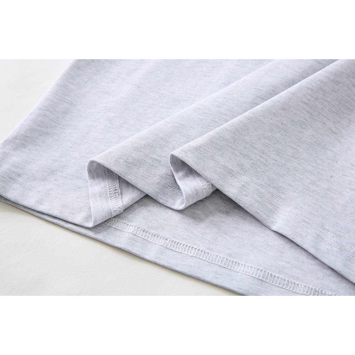Close-up of the light gray T-shirt's folded hem and visible stitching.