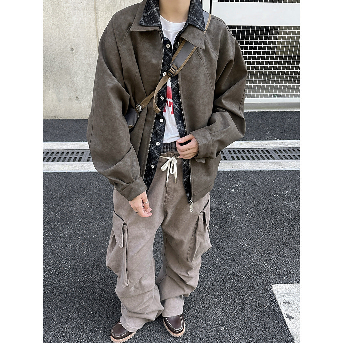 Model wearing a taupe zip-front jacket over a plaid shirt with loose gray cargo pants.