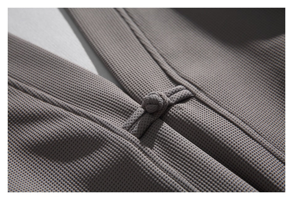 Close-up of a knotted frog closure and textured gray fabric on the jacket front.