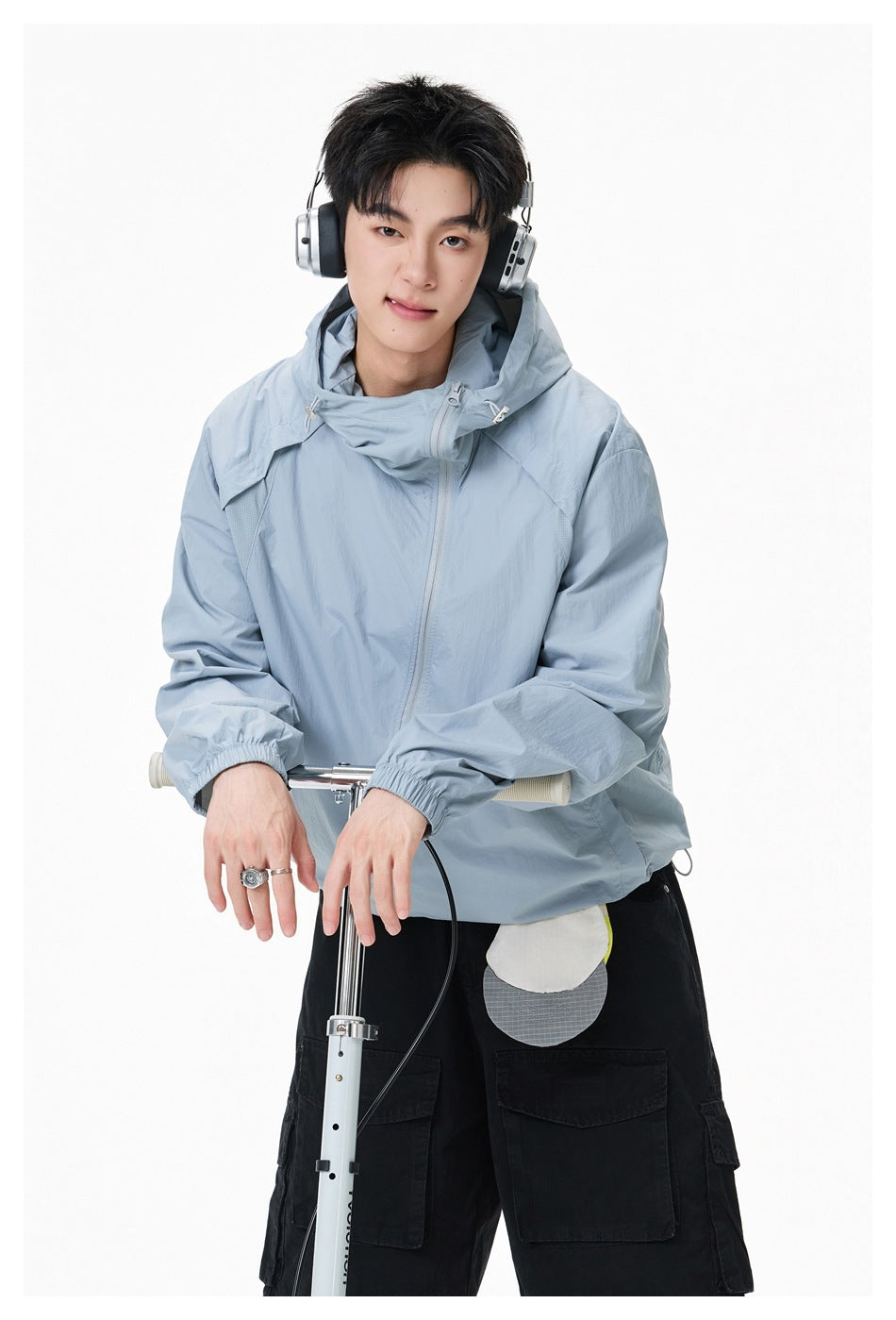 Closer view of a model in a pale blue hooded jacket and black cargo shorts, leaning on a scooter.