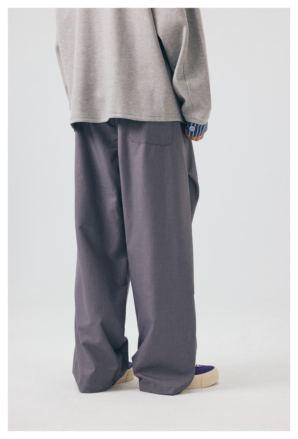 Rear view of a model wearing loose gray trousers and a light gray top, showing a back pocket.