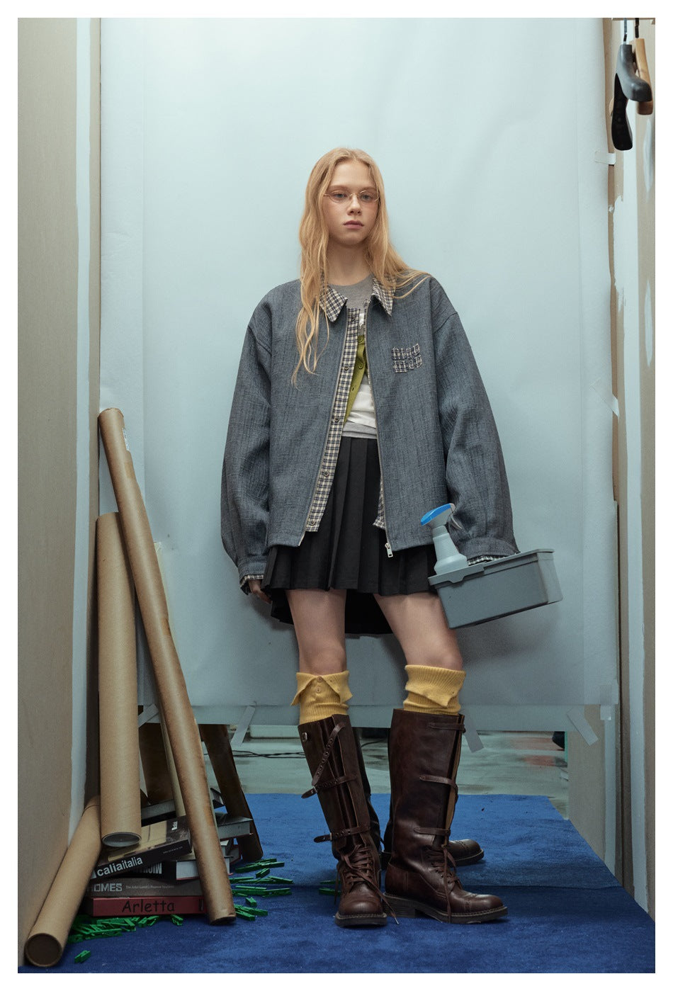 Front view of a model in an oversized blue-gray jacket with plaid trim and chest pocket, paired with a black skirt.