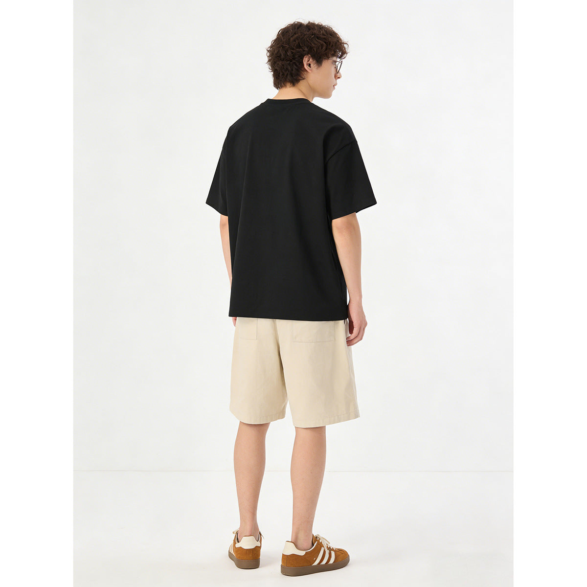 Rear view of a model wearing a black oversized T-shirt and light beige shorts with two back pockets.