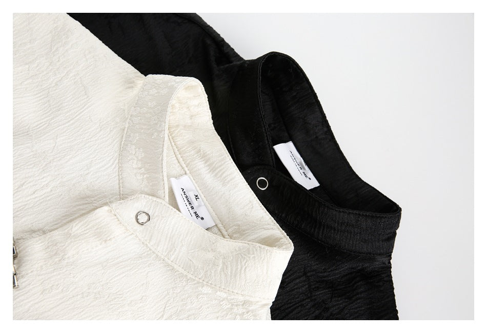Close-up of overlapping ivory and black garments showing raised texture, collar edges, and metal ring closures.