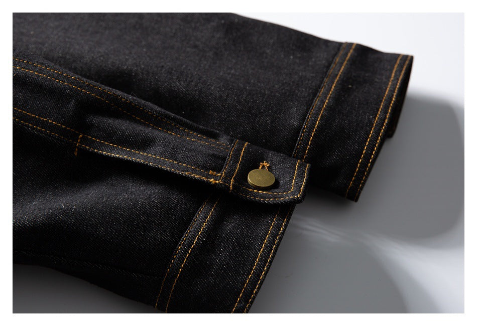 Close-up of a black denim sleeve cuff with a brass-colored button and golden double stitching.
