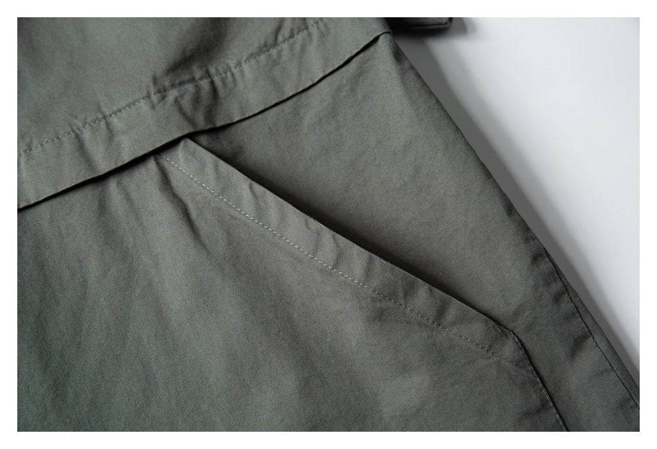 Close-up of a slanted pocket opening and stitched horizontal panel on a dark gray-green shirt.