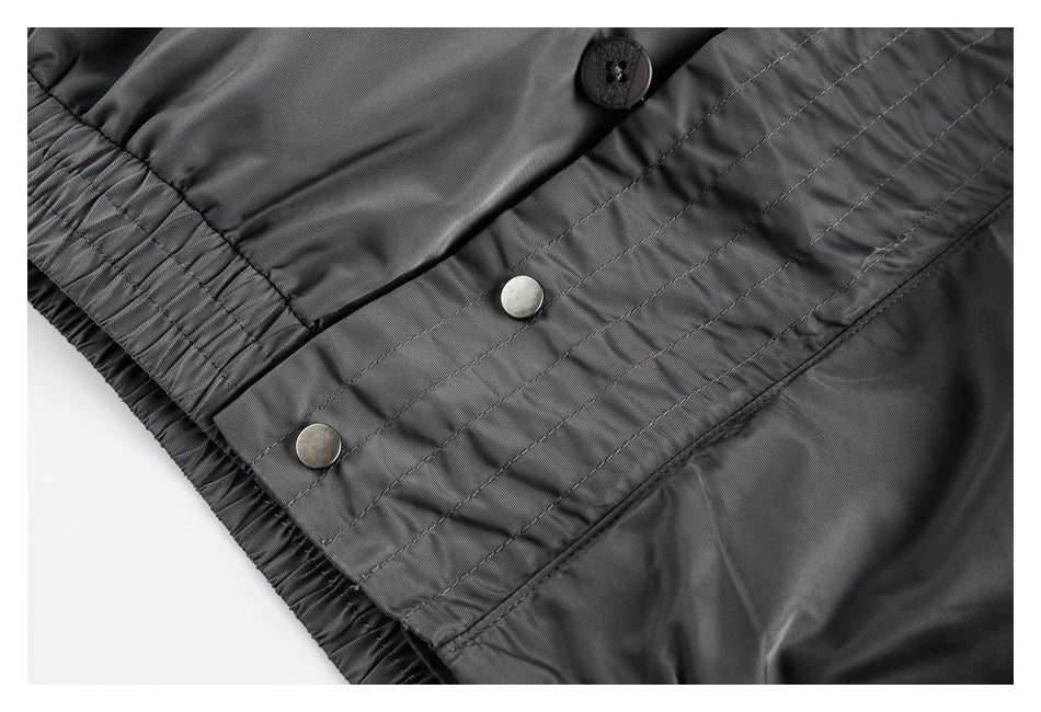 Close-up of a gray jacket's stitched lower placket, metal snaps, and gathered elastic edge.