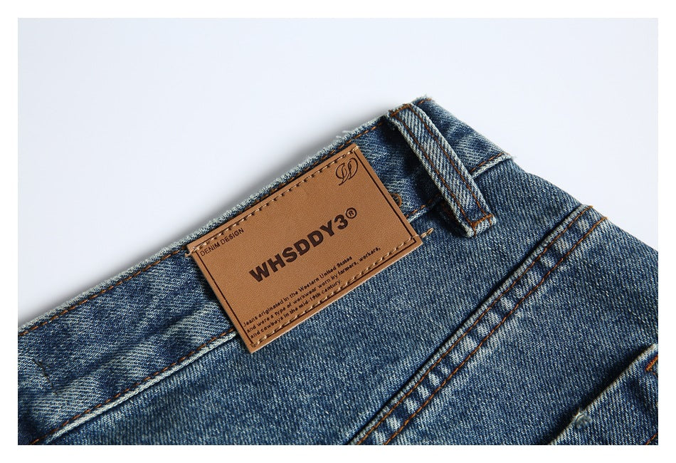 Close-up of blue denim jeans showing a brown waistband patch with dark lettering and orange stitching.