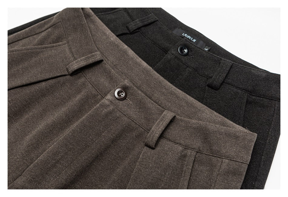 Close-up of brown and charcoal trouser waistbands showing buttons, belt loops, pleats and an inner garment label.