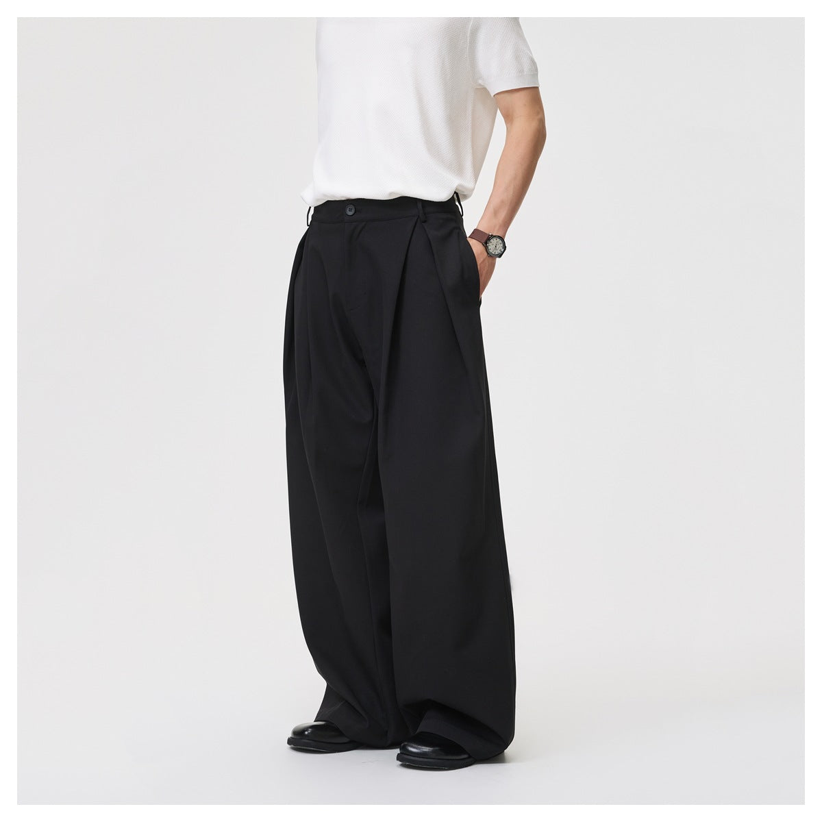 Model wearing black wide-leg pleated trousers with white top, hand in pocket, side view