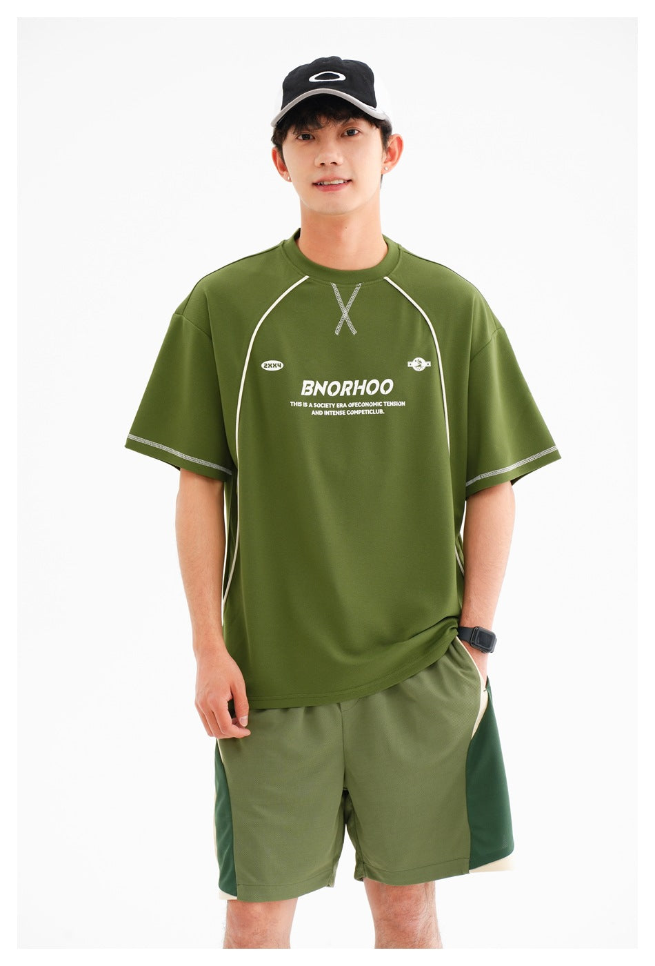 Close view of a model wearing an olive green athletic T-shirt with pale piping and matching color-block shorts.