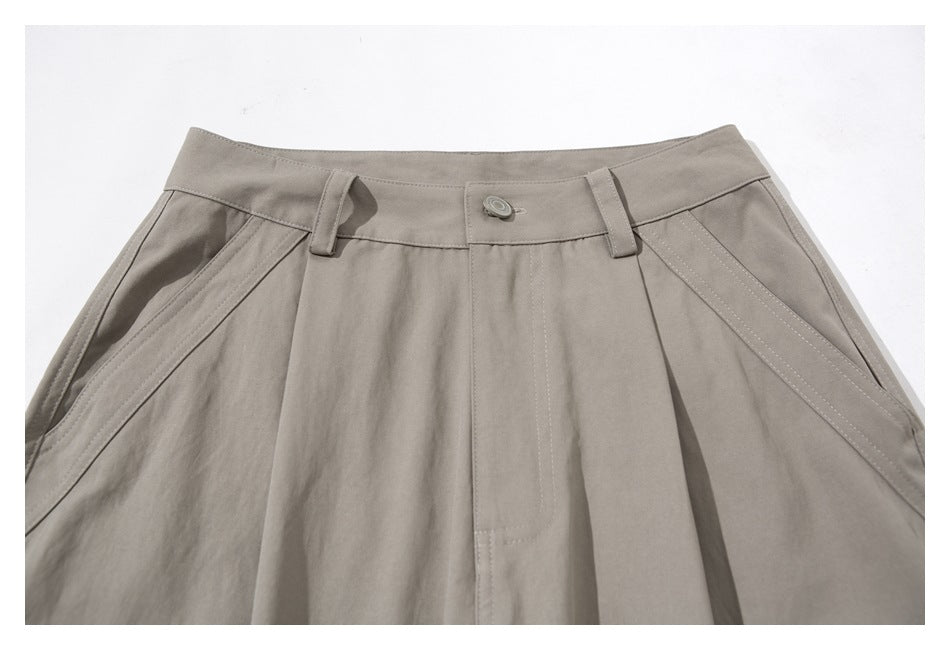 Close-up of taupe cargo pants showing the buttoned waistband, belt loops, pleats and angled front pockets.