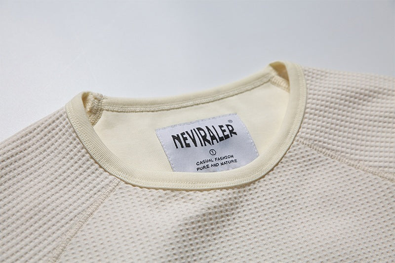 Close-up of the cream shirt's ribbed crew neckline and sewn-in brand label.