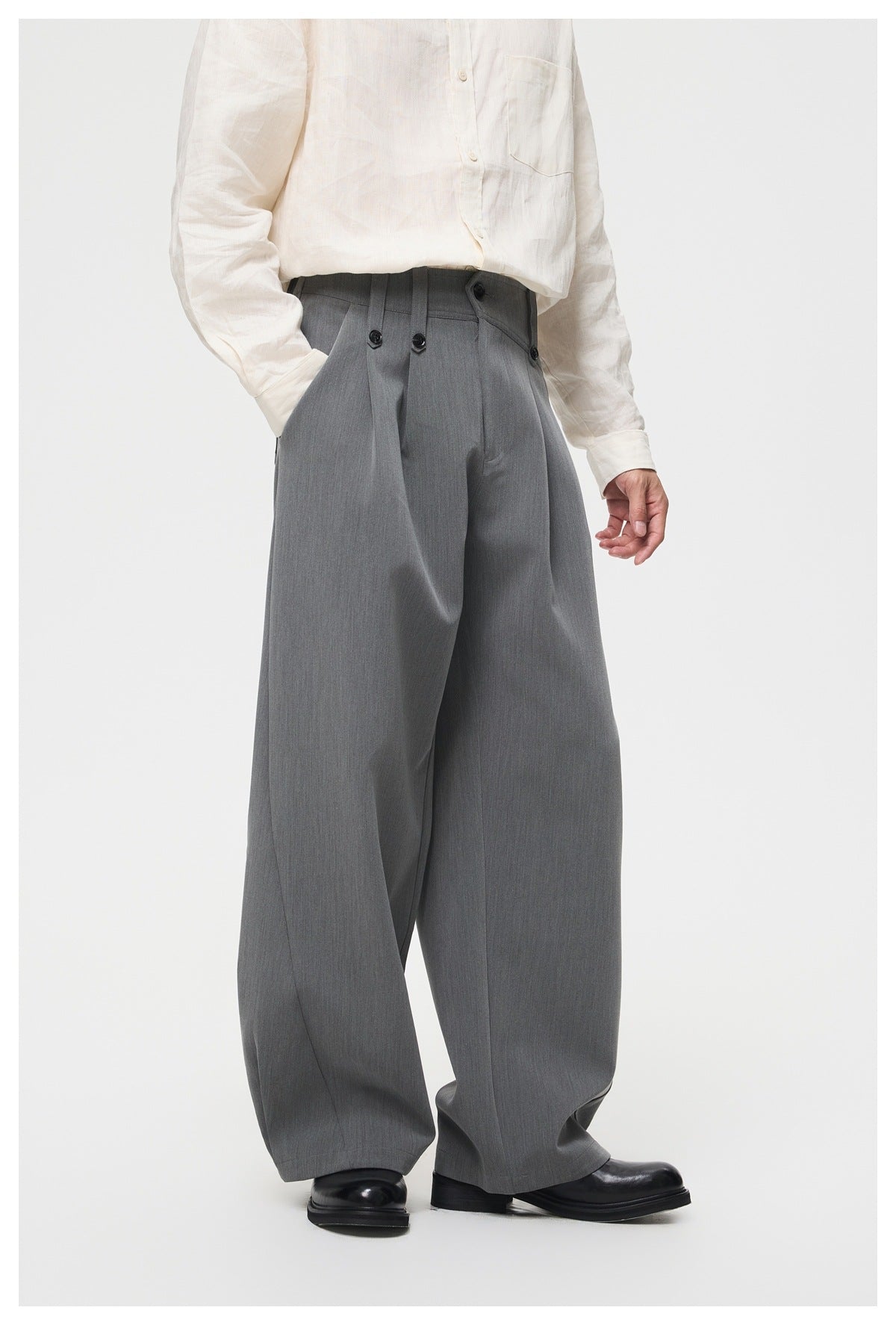 Model wearing gray wide-leg trousers with front pleats and button tabs, angled three-quarter view