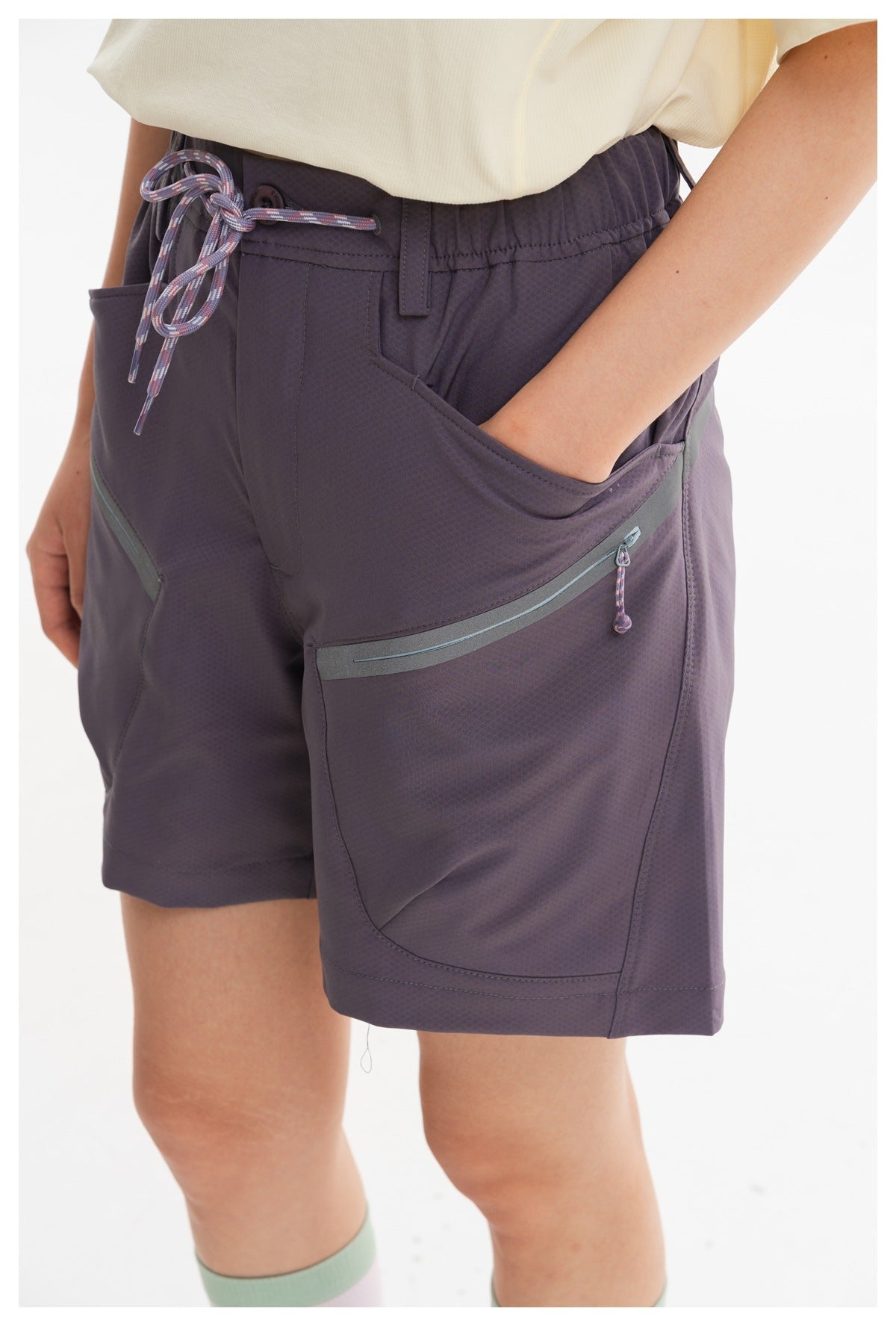 Close-up of dark purple shorts showing a drawstring waist, hand pocket, and zippered side pocket.