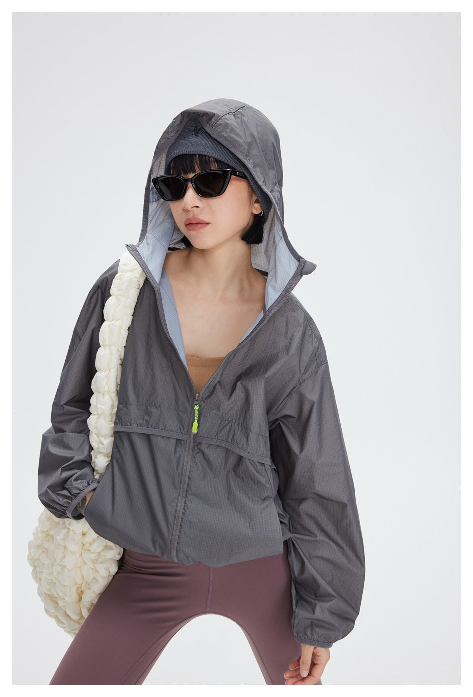 Model wearing the gray windbreaker with its hood up, mauve leggings and sunglasses, shown from the front.