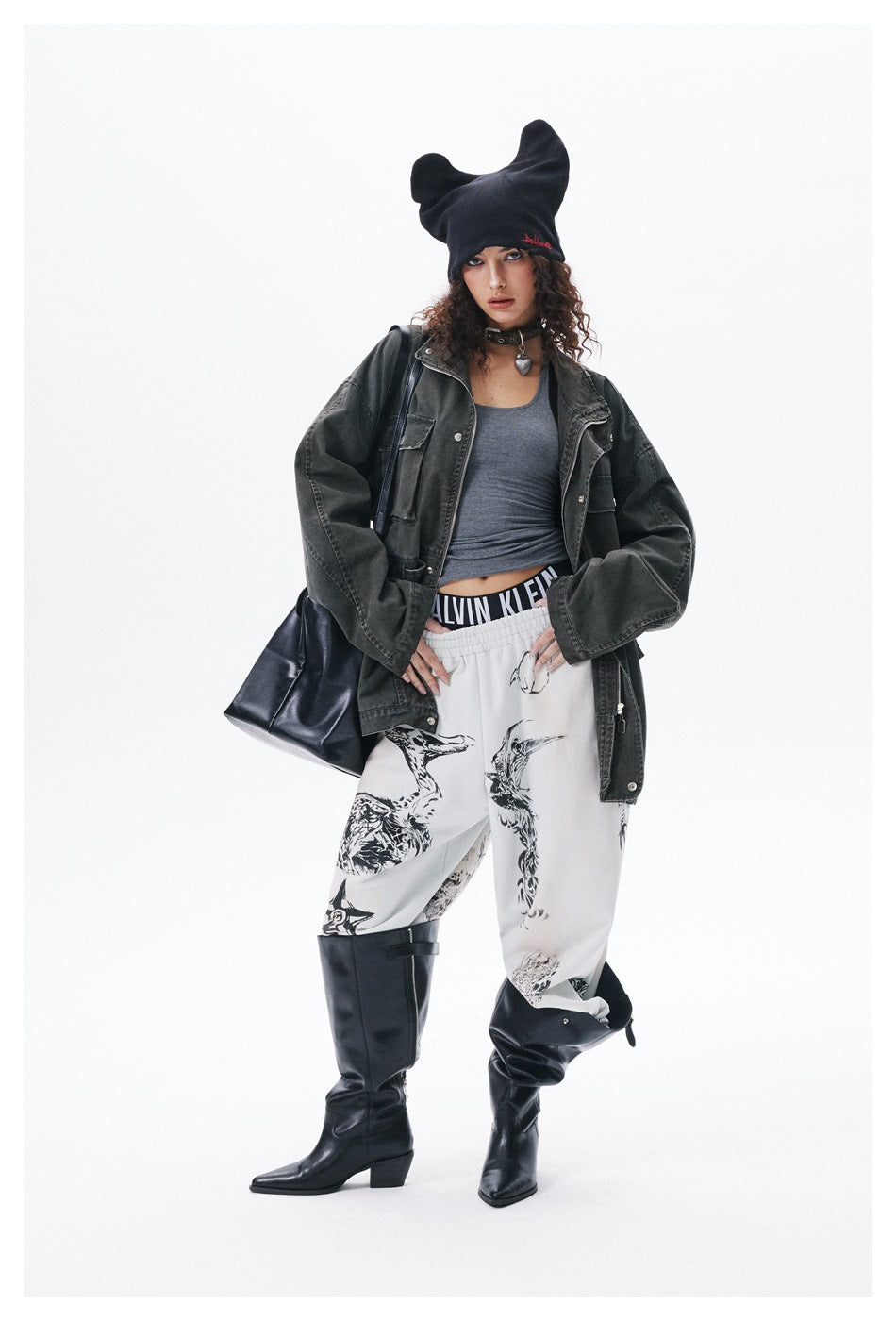 Model with hands on hips wearing an oversized dark green utility jacket open over a gray tank top