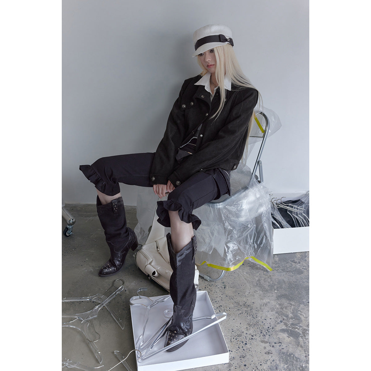 Seated model wearing a black buttoned jacket with ribbed sleeves and cropped ruffle-hem trousers.