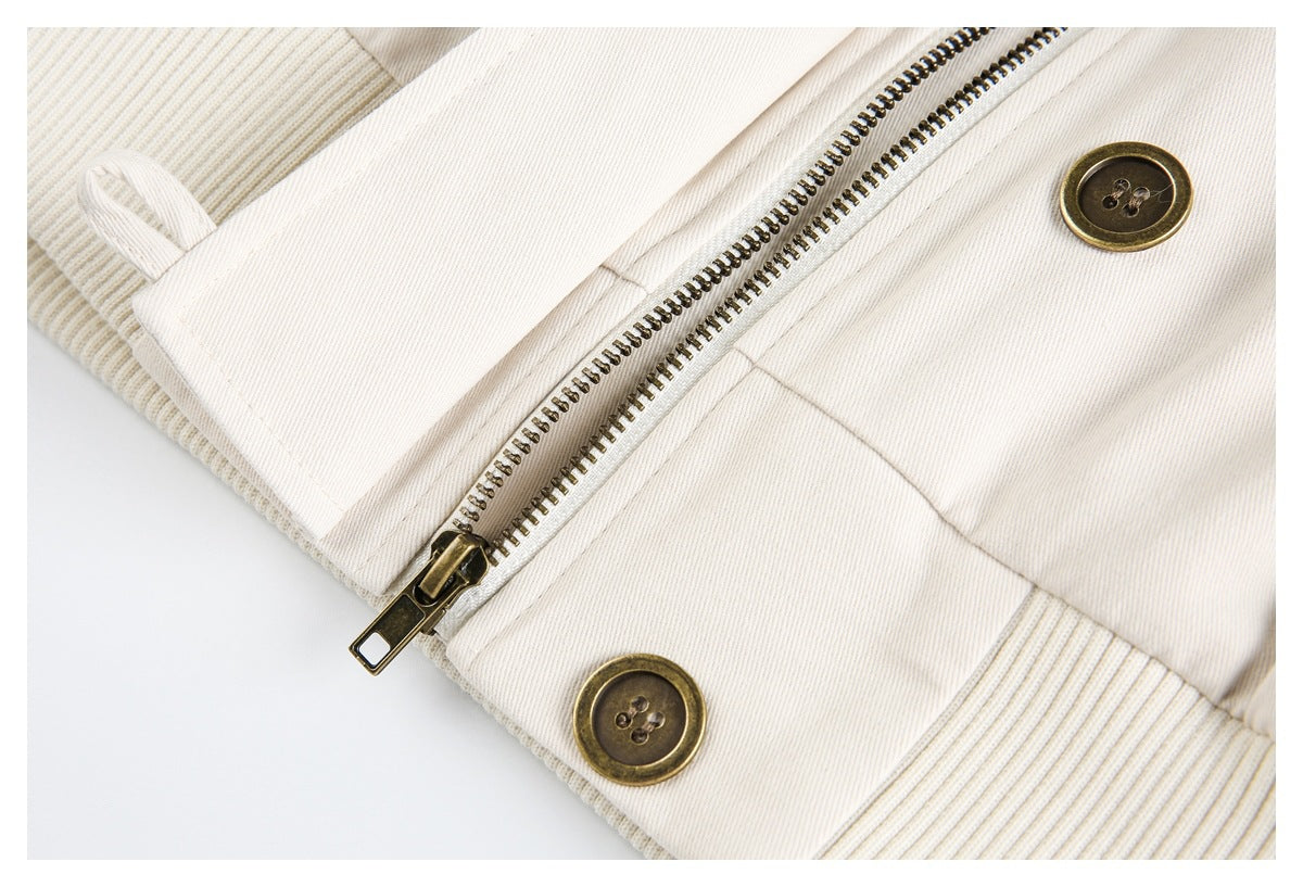 Close-up of an ivory jacket's brass-colored zipper, buttons, and ribbed hem.
