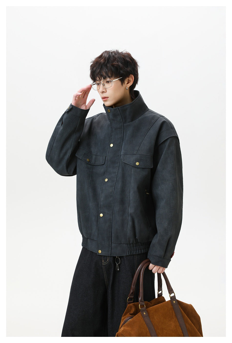 Model wearing a dark charcoal jacket with a stand collar, brass-tone buttons, two flap chest pockets, and an elastic hem.