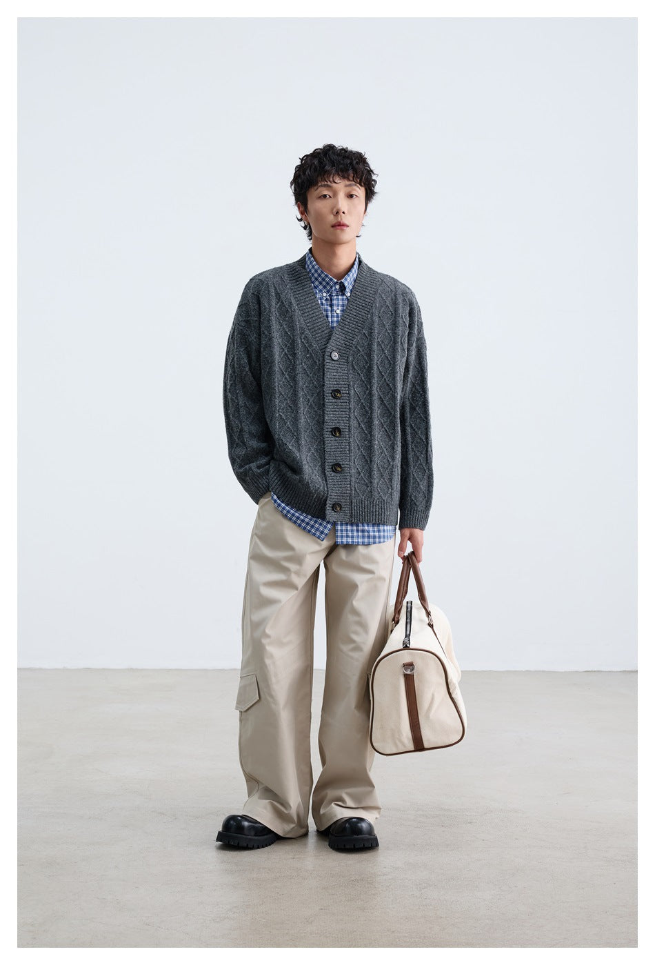 Front view of a model in a charcoal gray cable-knit button cardigan over a blue checked shirt.