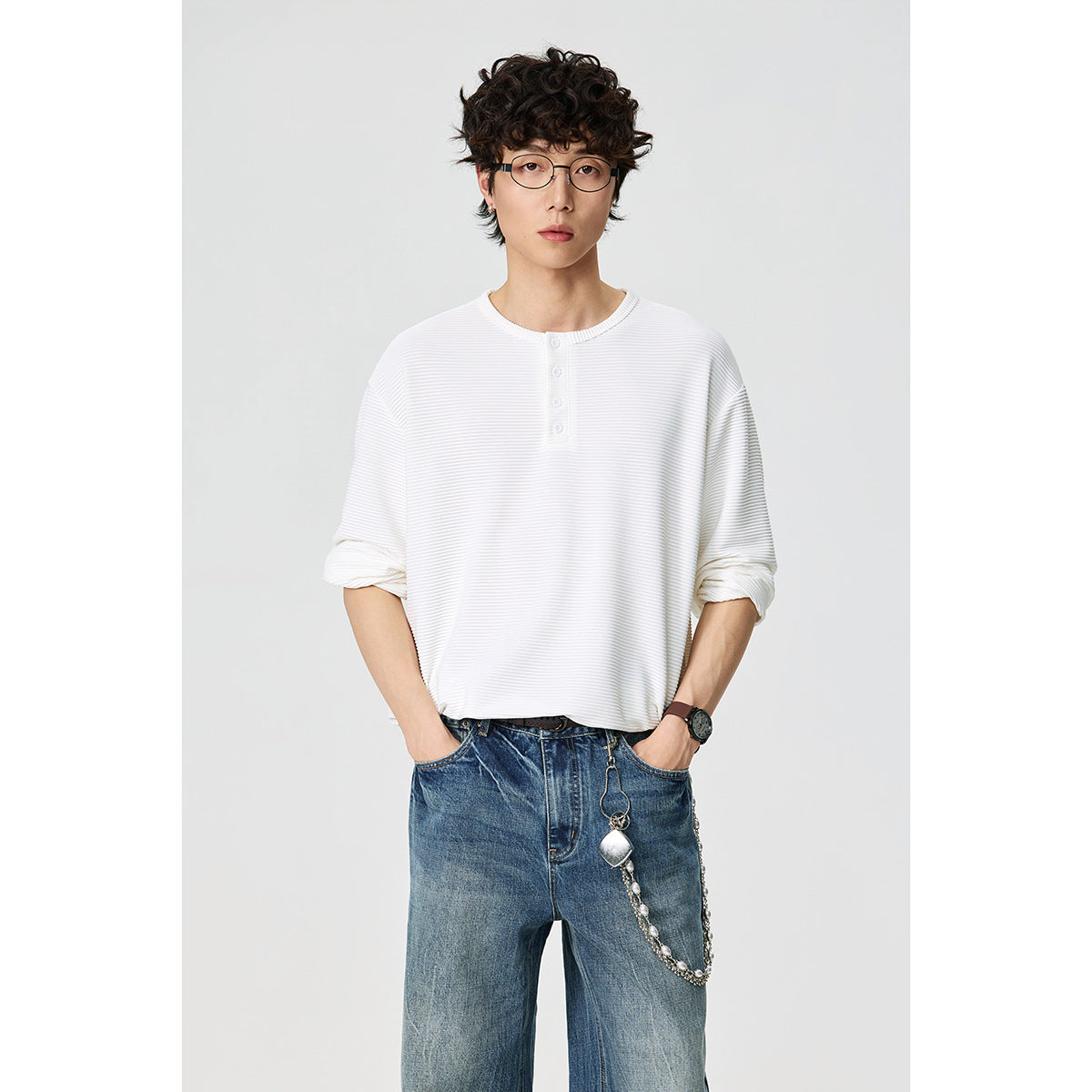 Front view of a model wearing a white long-sleeve ribbed henley shirt with a short button placket.
