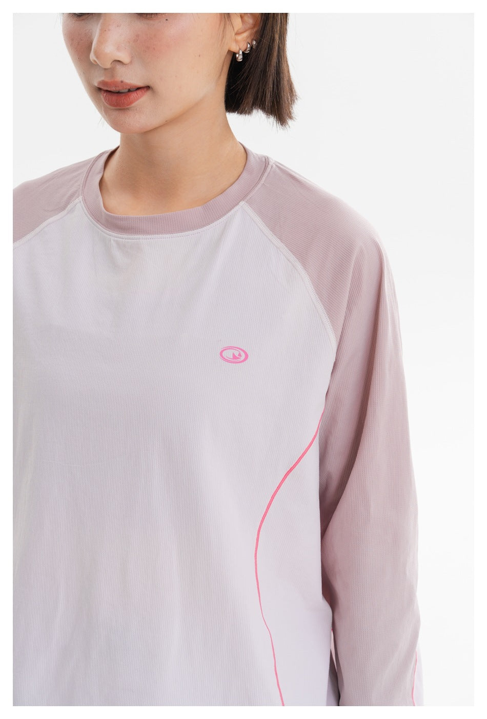 Close-up of the pale pink and white top, showing its raglan seams, ribbed neckline, pink piping, and small chest emblem.