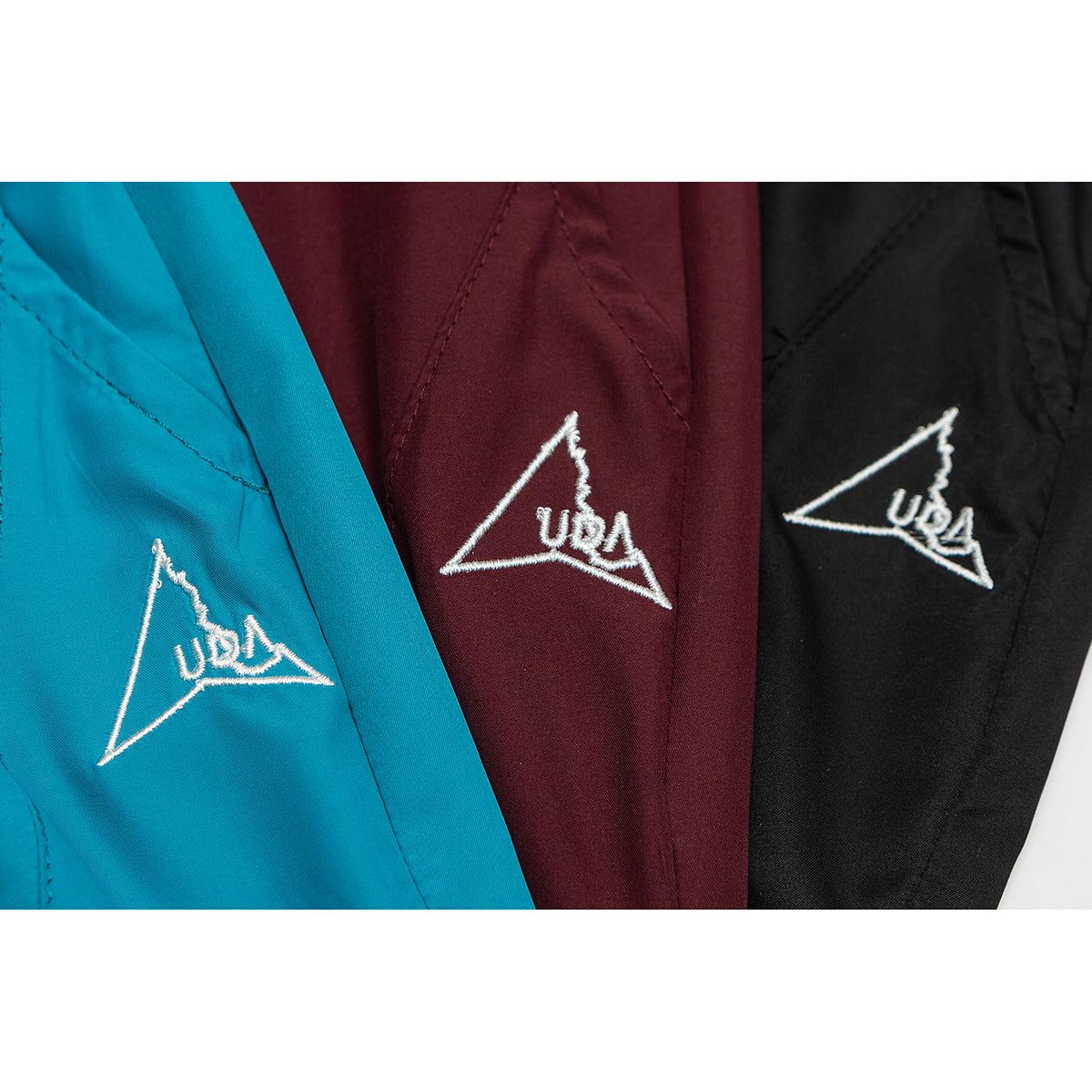 Close-up of embroidered triangular emblems on turquoise, burgundy, and black shorts.