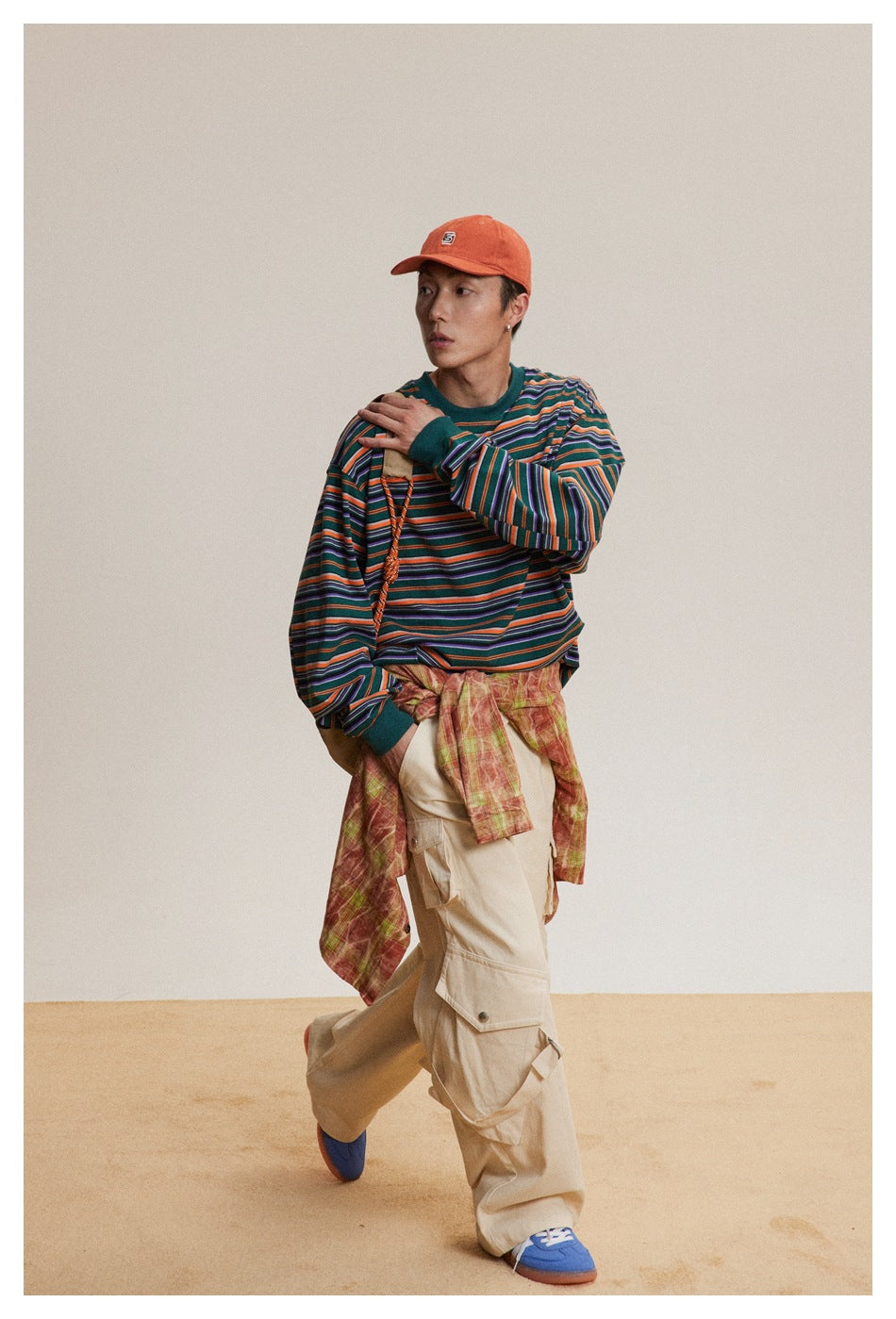 Full-length model wearing a teal, orange, purple and white striped shirt with loose beige cargo pants and an orange cap.