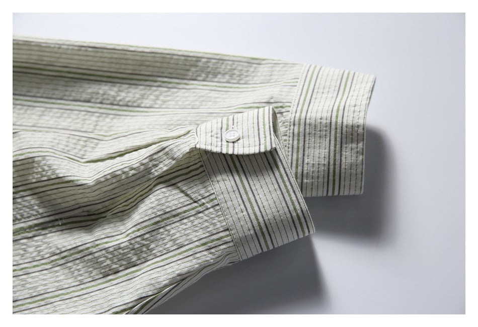 Close-up of a white shirt cuff with a button, patterned with narrow green and gray stripes.