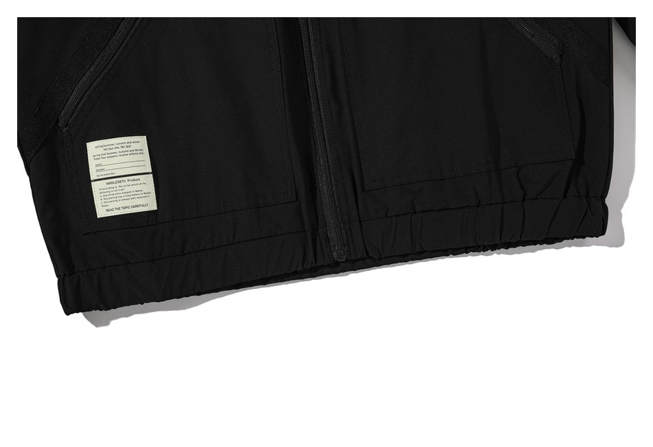 Close-up of the black jacket's lower front, showing the zipper, pockets, elastic hem, and a small label.