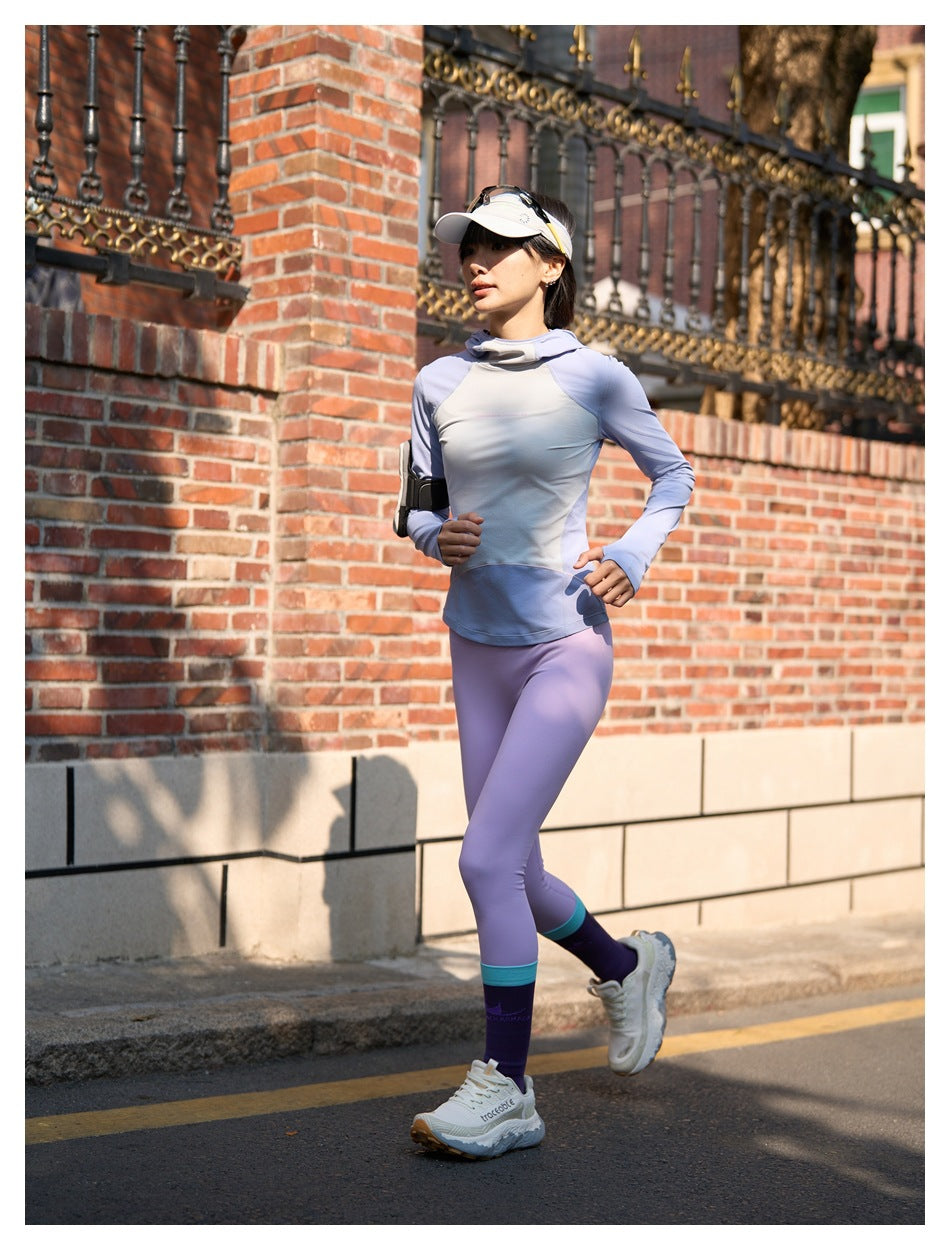 Woman running in a pale blue long-sleeve top and lavender leggings with purple socks.